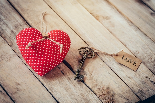 Heart fabric and vintage key with tag label LOVE on wood table background.