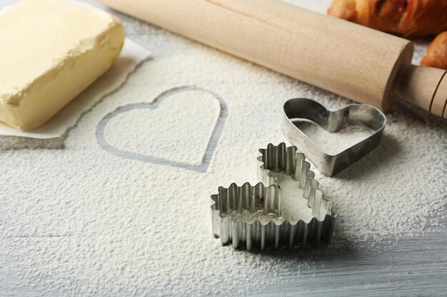 Heart of flour, croissant and  wooden kitchen utensils on gray background