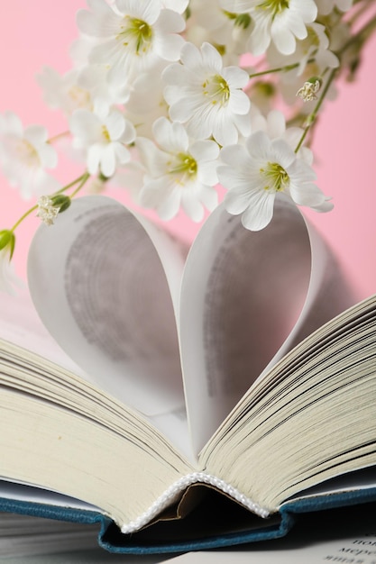 Heart from book pages and flowers on pink background close up