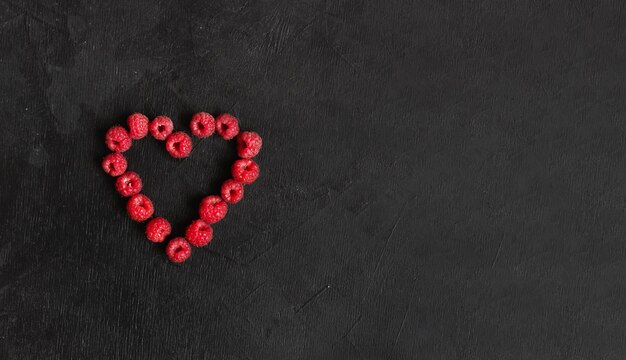 Photo the heart from the raspberies on the black background with copyspace