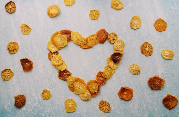 Foto cuore di chips di frutta incorniciato con pezzi di frutta secca su uno sfondo blu graffiato