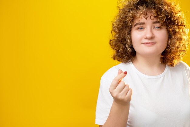 Gesto del cuore ama te stesso accettazione del corpo giovane donna in sovrappeso sorridente soddisfatta con capelli ricci isolati su sfondo giallo spazio copia