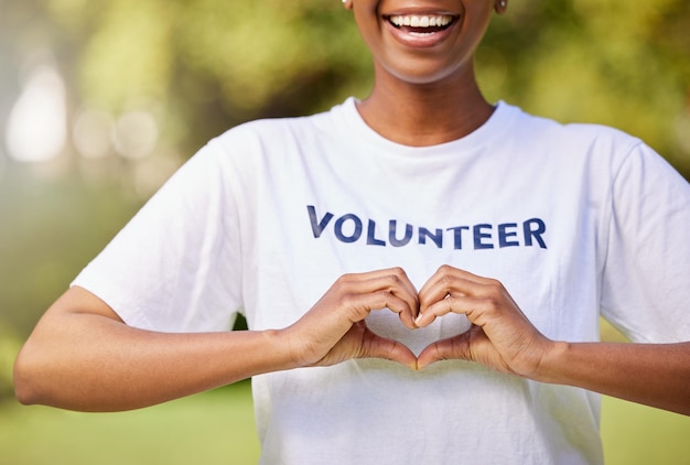 Mani a cuore e sorriso volontario con cartello per supporto assistenziale e beneficenza all'aperto nella natura, foresta o ambiente mostra amore e persona felice che fa volontariato nella comunità o nel servizio con empatia