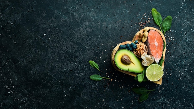 Heart health foods salmon avocados blueberries broccoli nuts and mushrooms On a black stone background Top view Copy space