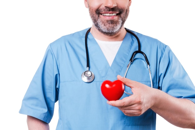 Heart in his hand. Close-up of mature cardiology surgeon holding heart shape toy and smiling while standing isolated on white