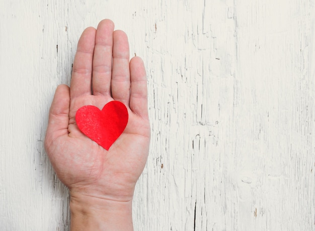 Heart in human hand. White wood surface. Retro tinted.