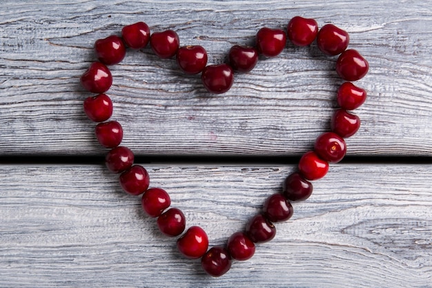 Heart made of cherries fruit on gray wooden background keep your heart healthy wealth of the garden