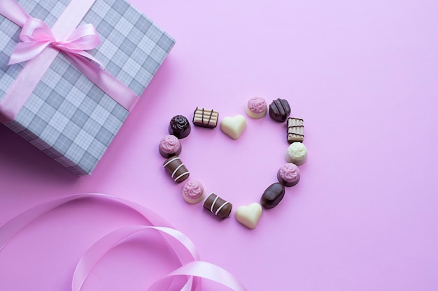 Heart made of chocolate pralines on pink background Image with copy space