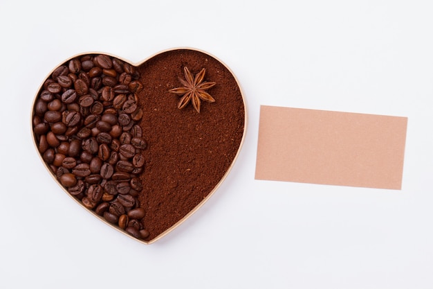 Heart made of coffee grains and instant coffee powder. Blank paper for copy space. White isolated surface .