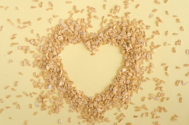 Heart made from oat groats on pastel yellow background