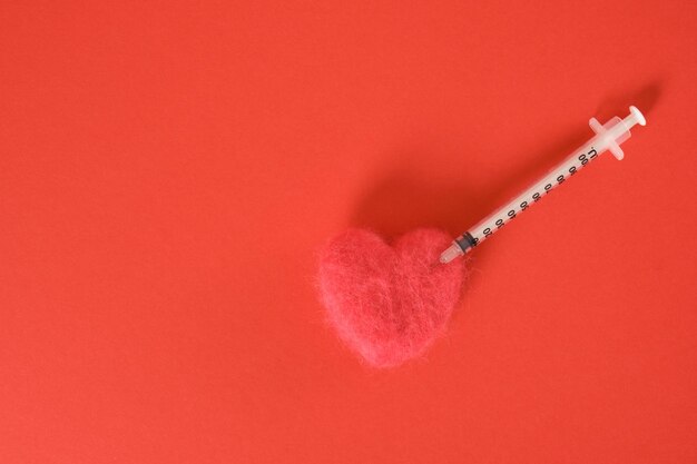 A heart made of natural wool and a syringe on a red background