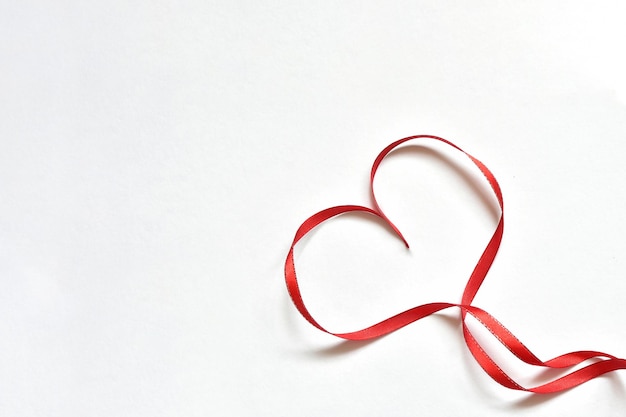 Heart made of thin red satin ribbon laid out on a white background