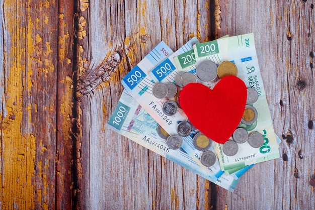 Heart next to a pile of Mexican pesos on a wooden table Cost of health concept