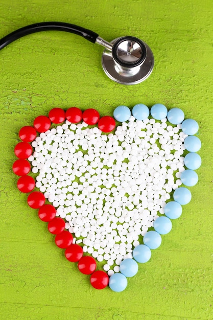 Heart of pills and stethoscope on wooden background