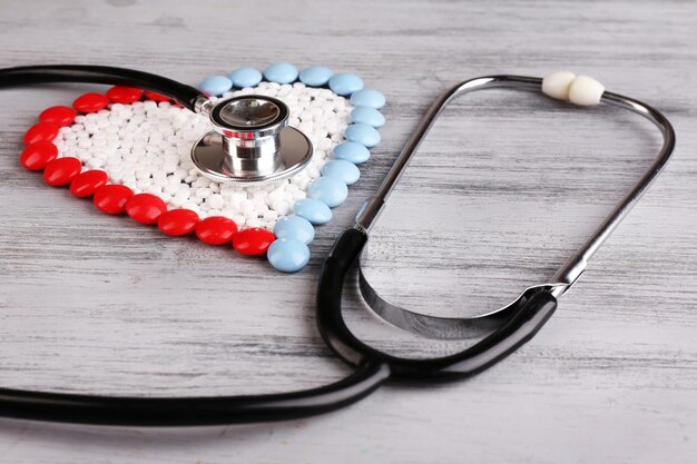 Heart of pills and stethoscope on wooden background