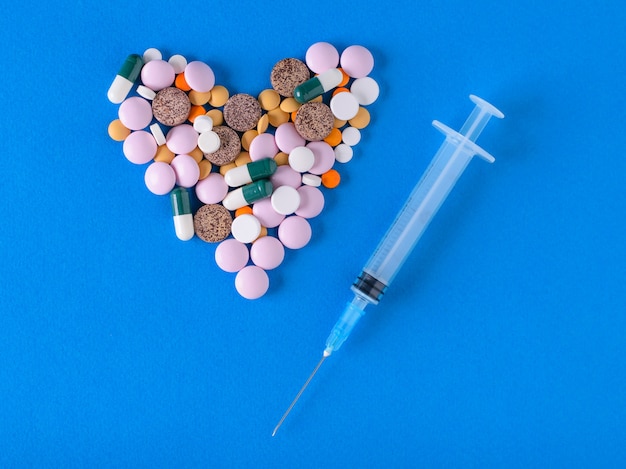 Heart of pills and syringe with needle on blue background.