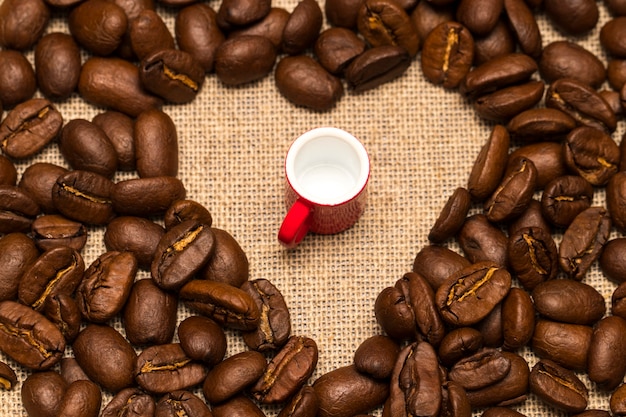 Heart of roasted coffee beans and a Cup on burlap background