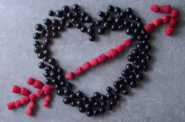 Heart shape and arrow made with fresh raspberries and black currants. Top view grey table