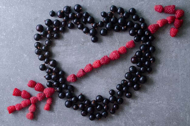 Forma di cuore e freccia fatta con lamponi freschi e ribes nero. tavolo grigio vista dall'alto