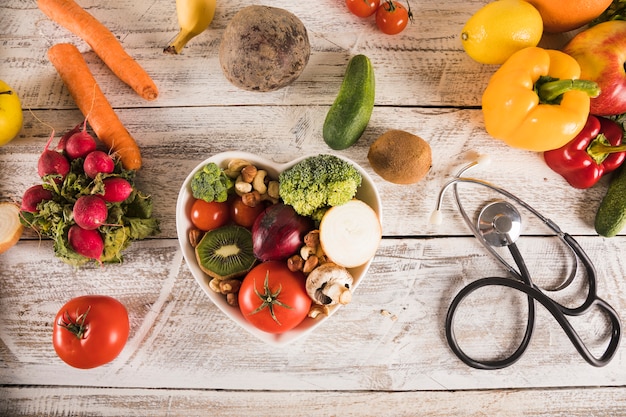 Heart shape container with healthy vegetables near stethoscope