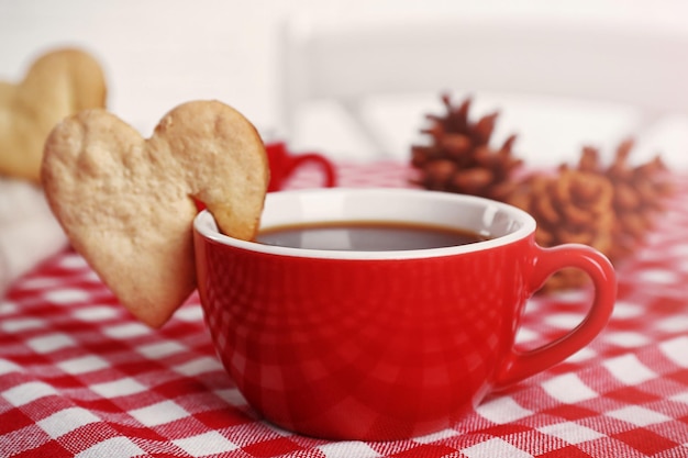 Heart shape cookie on cup of coffee on checkered napkin closeup