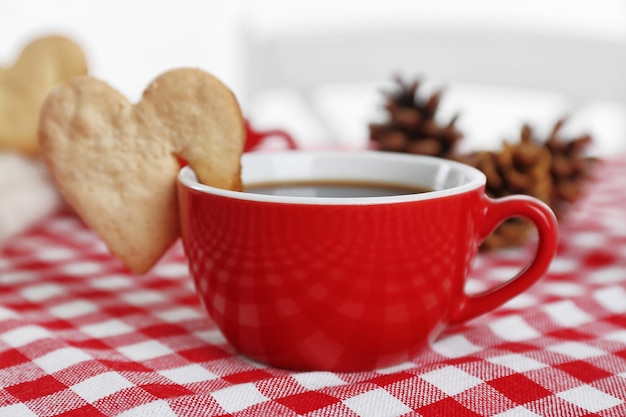 Heart shape cookie on cup of coffee on checkered napkin closeup