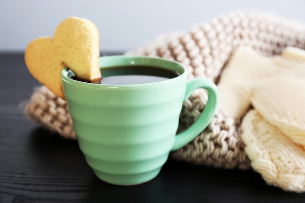 Heart shape cookie on cup of coffee on wooden table closeup