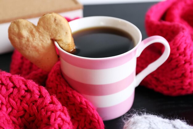 Heart shape cookie on cup of coffee on wooden table closeup