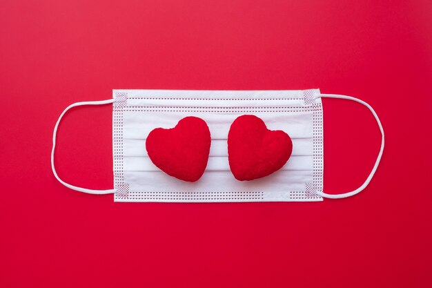 Heart shape decoration and medical face mask on red background against coronavirus disease infection