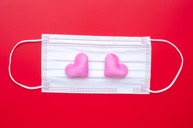 Heart shape decoration and Medical face mask on red background against Coronavirus disease infection.