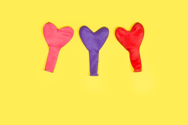 Heart shape deflated colored balloons on a yellow background with copy space