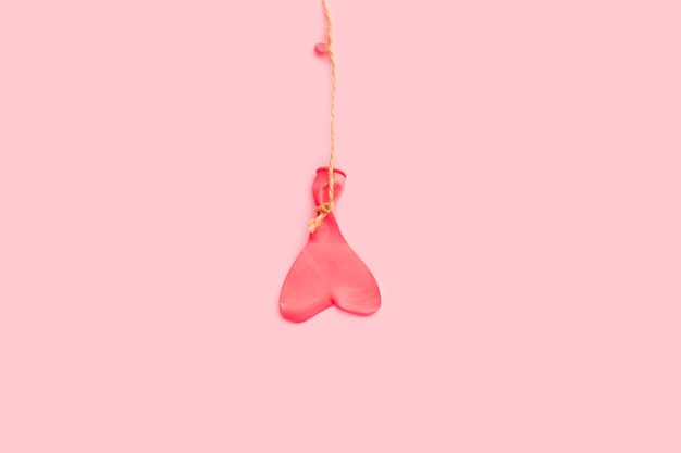 A heart shape deflated pink balloon hanging from a sisal thread