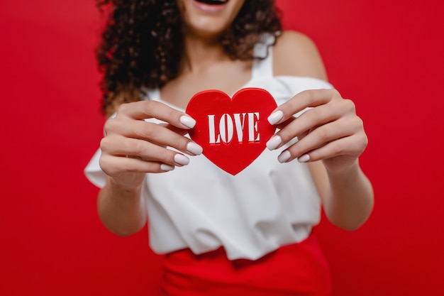 Foto figura a forma di cuore con lettere d'amore nelle mani della donna di colore sulla parete rossa