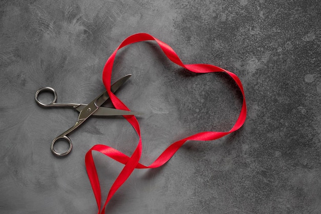 Фото Форма сердца из красной ленты и ножниц на темном фоне