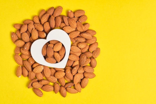 Heart shape and handful of almonds yellow background