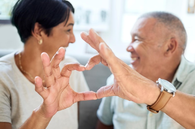 Heart shape hands and senior couple bonding and talking in the living room of their home Happy smile and closeup of an elderly man and woman in retirement with a love sign or gesture together