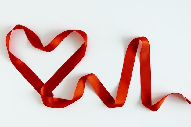 심장 모양과 심장 박동수는 흰색 배경에 빨간색 새틴 리본으로 줄 지어 있습니다. 사랑, 의학 및 생명 보험 개념입니다. 광고 전단지. 텍스트에 대 한 장소입니다. 격리.