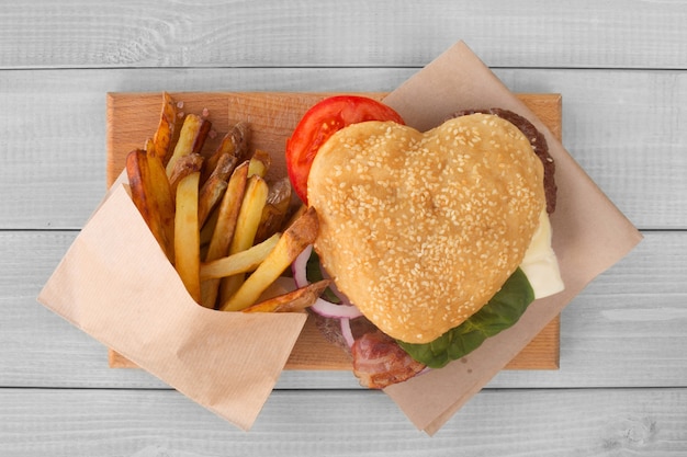 ハート形の愛のハンバーガーとフライドポテト、ハンバーガーファーストフードのコンセプト、バレンタインデーのサプライズディナー、木製の背景、上面図フラットレイ