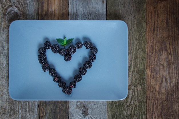 Heart shape made from blackberry berries on a gray plate on a wooden table