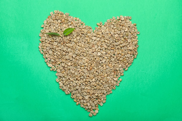 Heart shape made of green coffee beans on color