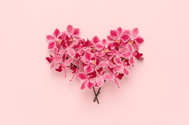 Foto a forma di cuore fatta di bouquet di fiori di orchidea su sfondo rosa di san valentino. disposizione piatta.