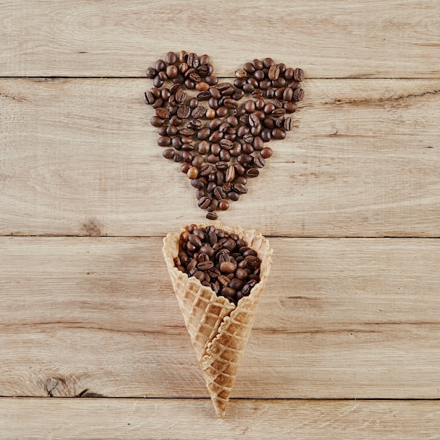 Heart shape make by roasted coffee been from waffle cone on wooden