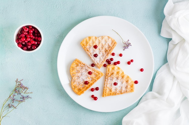 Heart shaped Belgian waffles with red berries and powdered sugar on a plate on the table. Valentine's Day. Top view. Copy space