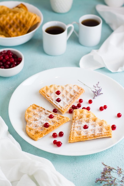 Heart shaped belgian waffles with red berry and powdered sugar\
on a plate on the breakfast table. valentine\'s day. vertical\
view