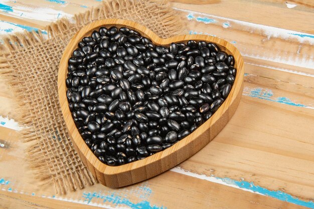Чаша из черной фасоли в форме сердца на деревянном столе
