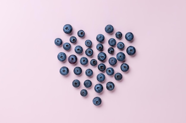 Heart shaped blueberries on color background