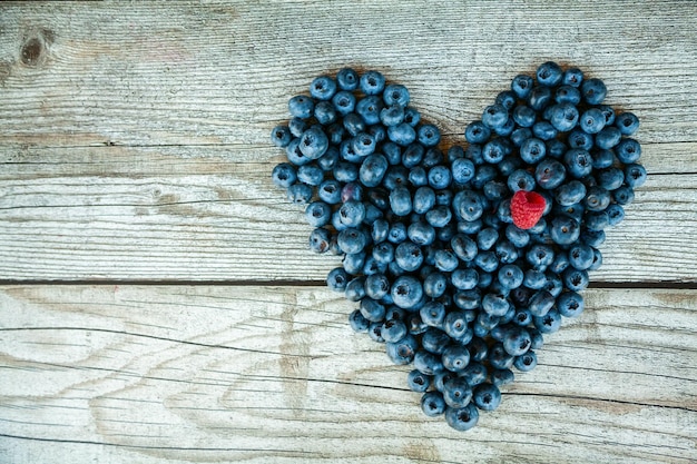 Heart shaped blueberries with one raspberry on a wooden background