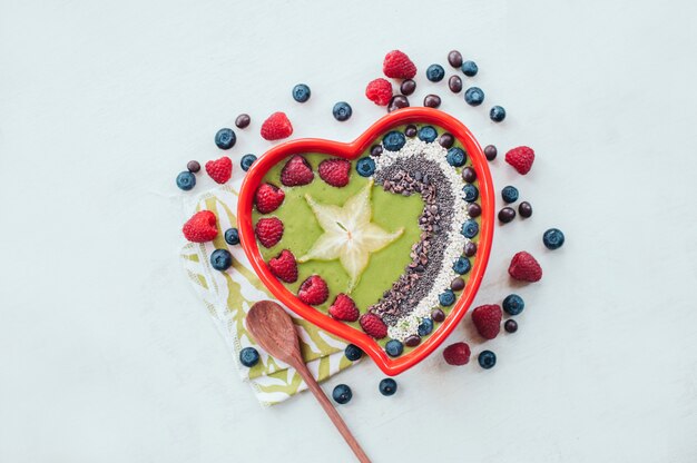 Heart shaped bowl of raspberry, blueberry, cocao nibs, wooden spoon near