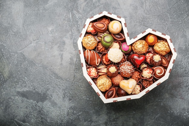 Heart-shaped box with delicious candies on grey background