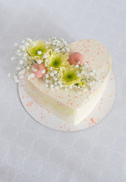 Heart-shaped cake decorated with fresh flowers on a white tablecloth